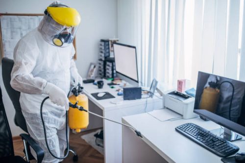 One man, man in protective suit disinfecting office work space alone.
